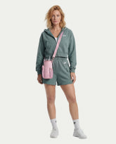 Woman wearing a green hoodie and shorts, holding a Magnetic Insulated Tumbler in a pink carrier sleeve.